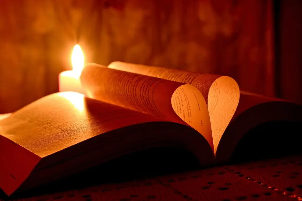 An open book with the pages folded into a love heart, a candle is lit in the background.